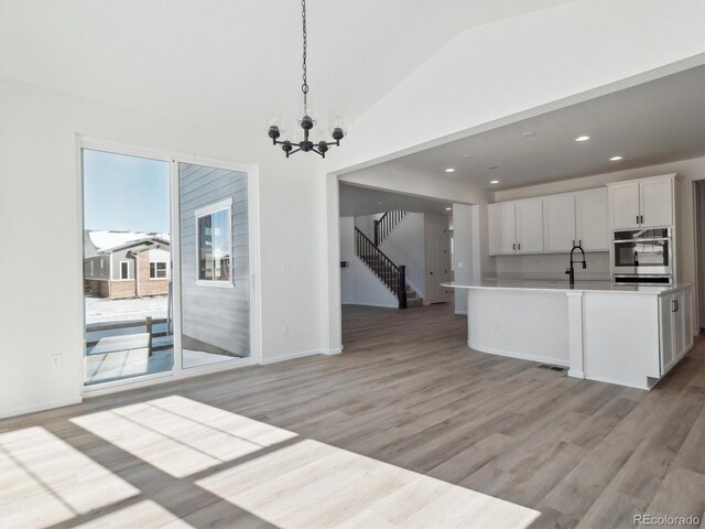 kitchen with pendant lighting, white cabinets, vaulted ceiling, light hardwood / wood-style flooring, and a chandelier