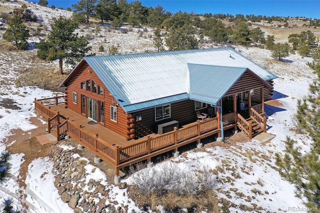 snow covered house featuring log exterior, metal roof, and a deck