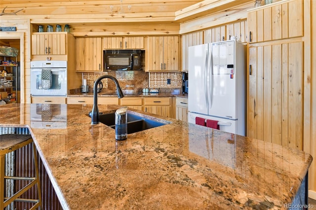 kitchen with backsplash, light brown cabinetry, light stone counters, white appliances, and a sink