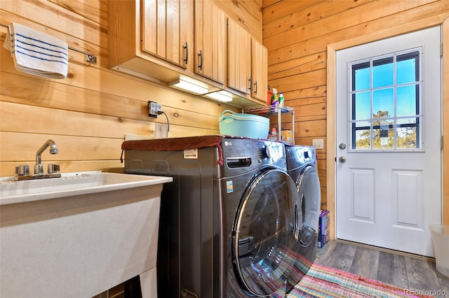 washroom featuring wooden walls, wood finished floors, cabinet space, a sink, and washer and clothes dryer