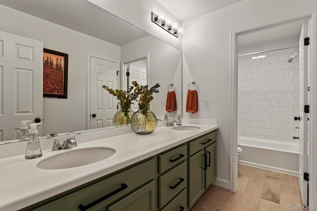 full bathroom featuring hardwood / wood-style flooring, vanity, tiled shower / bath combo, and toilet