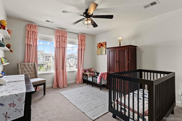 bedroom with a crib, light colored carpet, and ceiling fan