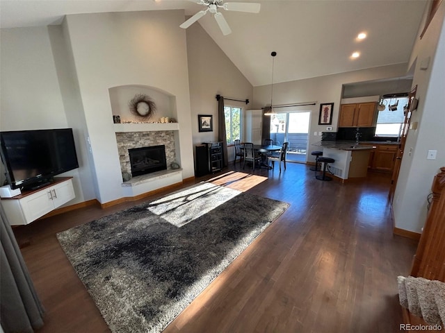 living room featuring a fireplace, high vaulted ceiling, ceiling fan, and dark wood-type flooring