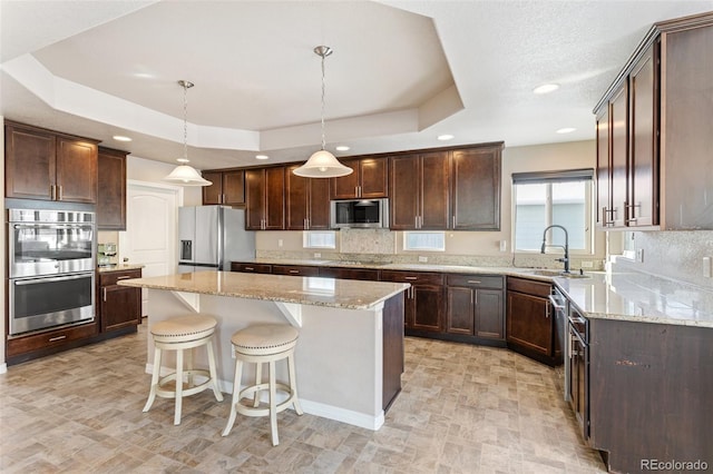 kitchen with hanging light fixtures, appliances with stainless steel finishes, a center island, and a raised ceiling