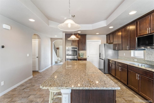 kitchen with dark brown cabinets, decorative light fixtures, light stone counters, a center island, and stainless steel appliances