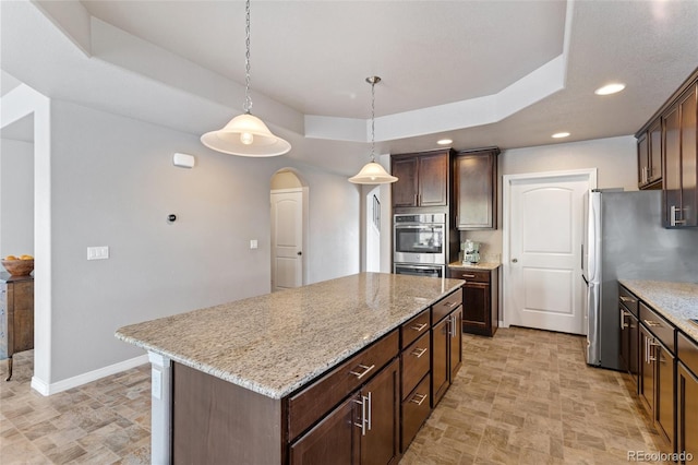 kitchen featuring decorative light fixtures, a center island, a raised ceiling, and dark brown cabinetry