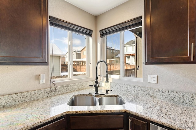 kitchen with sink, dark brown cabinets, stainless steel dishwasher, and light stone counters