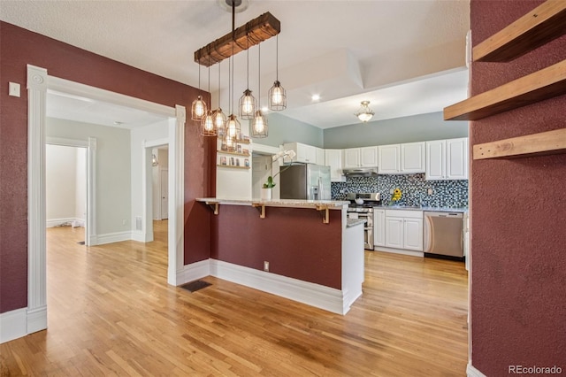 351 Bannock St, Denver, CO 80223 - kitchen with appliances with stainless steel finishes, a peninsula, a breakfast bar area, white cabinetry, and light wood finished floors