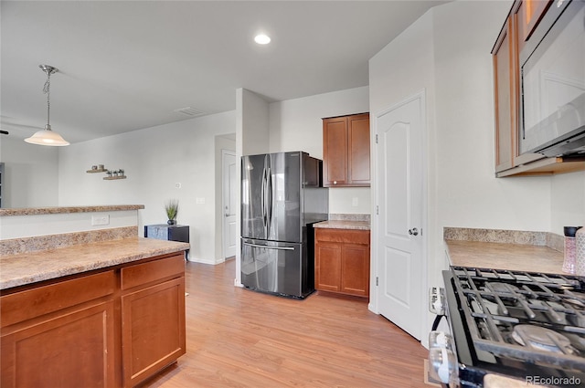 kitchen with gas range oven, refrigerator, hanging light fixtures, and light wood-type flooring