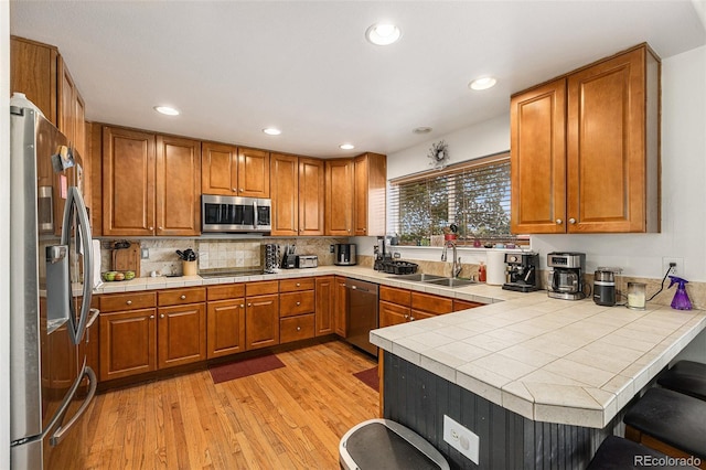 17464 Crestview Ct, Monument, CO 80132 - kitchen with stainless steel appliances, a peninsula, brown cabinetry, light wood finished floors, and backsplash