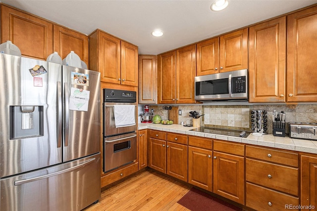 17464 Crestview Ct, Monument, CO 80132 - kitchen with stainless steel appliances, brown cabinets, light wood-style floors, backsplash, and recessed lighting