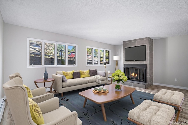 living room with a tile fireplace, wood-type flooring, a textured ceiling, and a baseboard heating unit