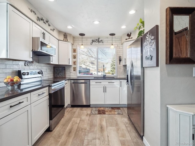 kitchen featuring range hood, stainless steel appliances, dark countertops, white cabinetry, and a sink