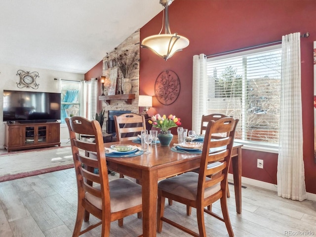 dining space featuring lofted ceiling, a fireplace, baseboards, and wood finished floors