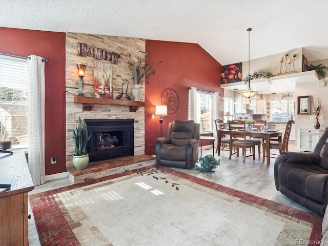 living area with lofted ceiling, a stone fireplace, a textured ceiling, and a wealth of natural light