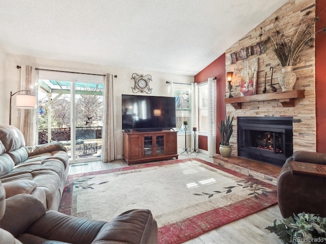 living room with a textured ceiling, vaulted ceiling, wood finished floors, and a stone fireplace