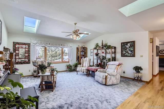 living room featuring a ceiling fan, vaulted ceiling with skylight, baseboards, and wood finished floors