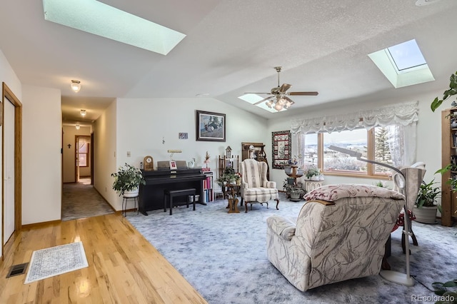 living room with vaulted ceiling with skylight, visible vents, a ceiling fan, wood finished floors, and a textured ceiling