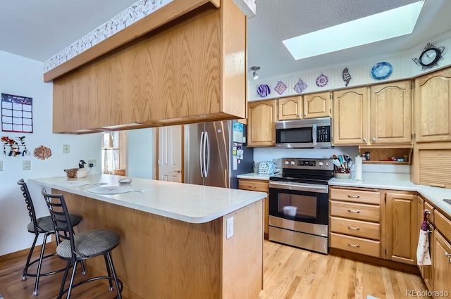 kitchen with a peninsula, a skylight, light wood-style floors, a kitchen breakfast bar, and appliances with stainless steel finishes