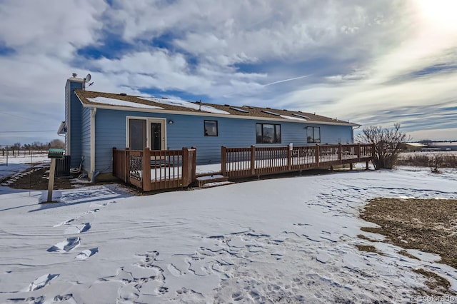 snow covered house featuring a chimney and a wooden deck