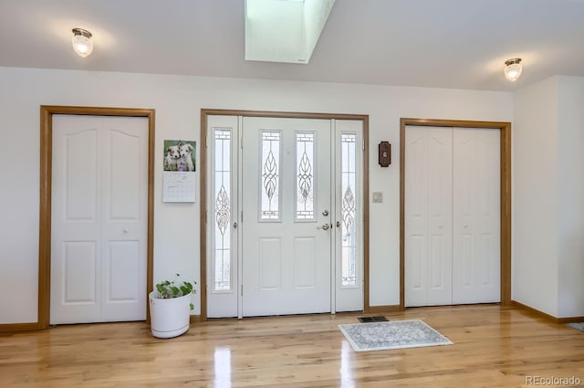 foyer entrance with baseboards, light wood-type flooring, and a skylight