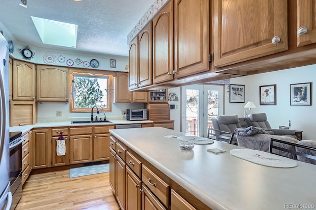 kitchen featuring light countertops, stainless steel electric range oven, light wood-style floors, a skylight, and a sink