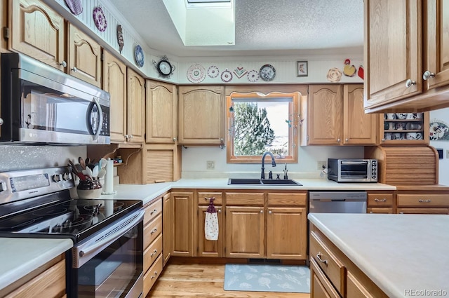 kitchen featuring light wood-type flooring, appliances with stainless steel finishes, light countertops, a sink, and a toaster