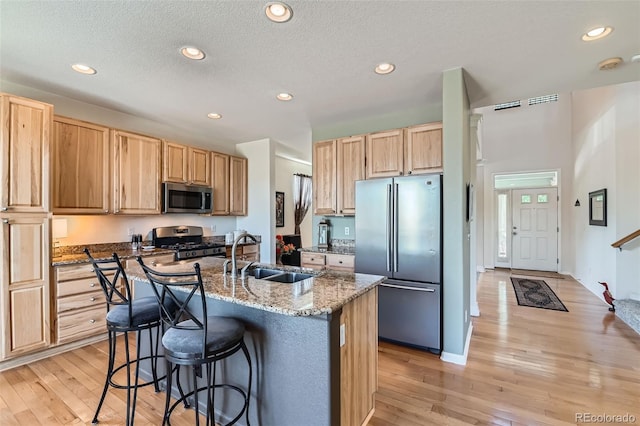 13962 Dexter Way, Thornton, CO 80602 - kitchen featuring appliances with stainless steel finishes, light brown cabinetry, a center island with sink, a kitchen bar, and recessed lighting