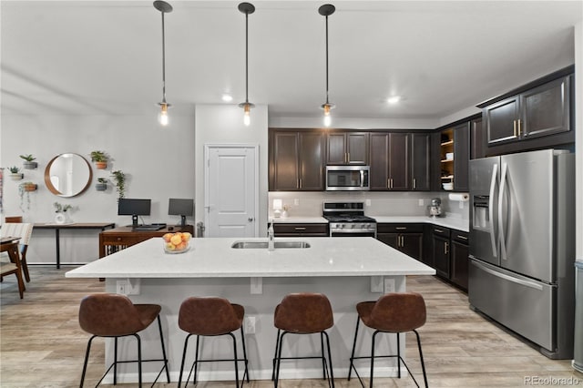 kitchen with stainless steel appliances, an island with sink, sink, and decorative light fixtures