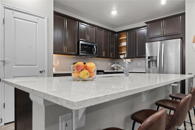 kitchen featuring dark brown cabinetry, stainless steel appliances, a breakfast bar, and a center island with sink