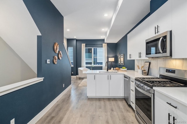 kitchen featuring backsplash, kitchen peninsula, light wood-type flooring, white cabinetry, and stainless steel appliances