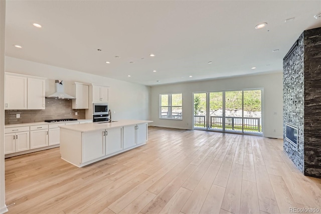 kitchen with white cabinetry, sink, backsplash, a center island with sink, and wall chimney exhaust hood