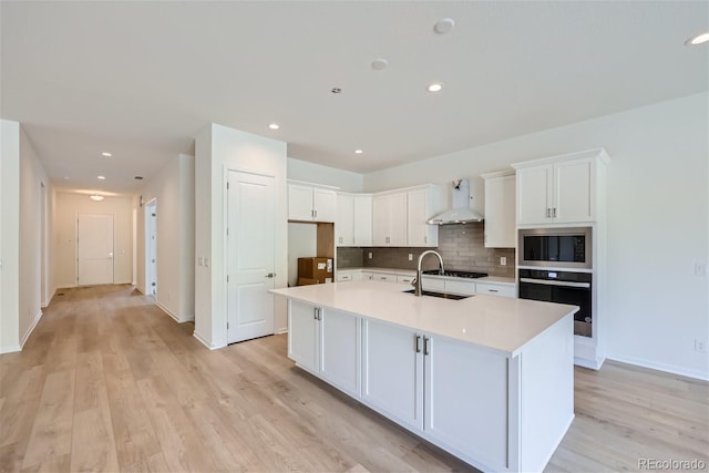 kitchen featuring built in microwave, white cabinets, a kitchen island with sink, and wall chimney range hood