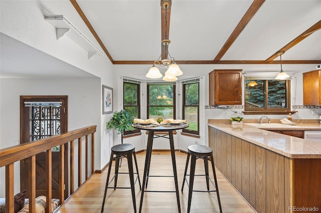 4677 S Wolff St, Denver, CO 80236 - kitchen with light wood-type flooring, brown cabinets, a chandelier, hanging light fixtures, and light stone countertops