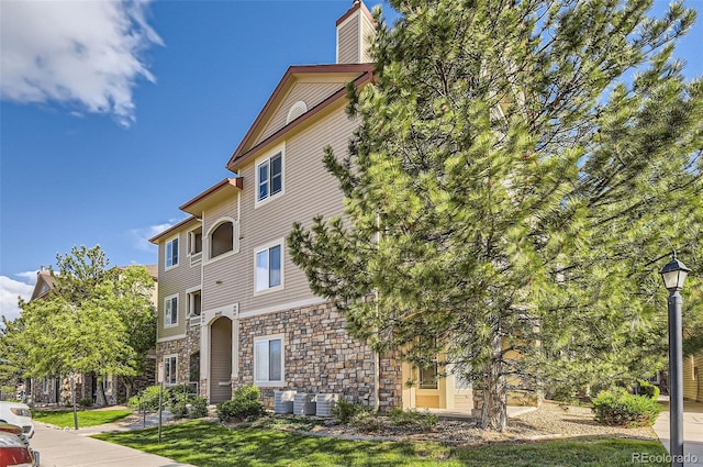 8445 S Holland Way Unit 205, Littleton, CO 80128 - view of side of home with stone siding, central AC unit, and a chimney