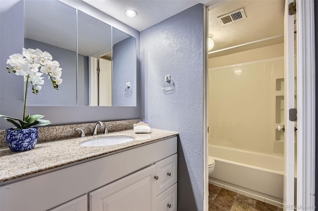 full bath featuring vanity, washtub / shower combination, visible vents, toilet, and a textured wall