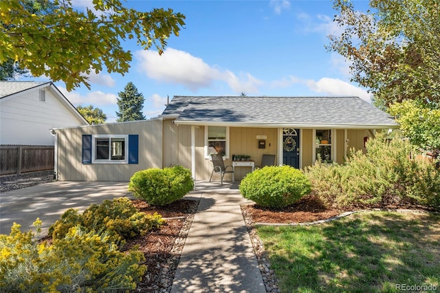 ranch-style home with roof with shingles, a porch, and fence