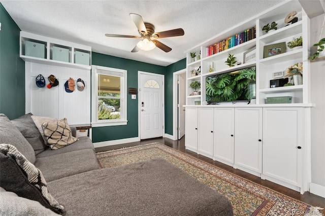 living room featuring a textured ceiling, dark wood-style floors, baseboards, and ceiling fan