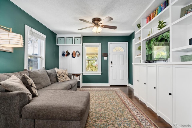 living room featuring baseboards, a textured ceiling, dark wood-type flooring, and a ceiling fan