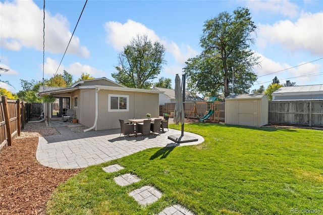 view of yard with a fenced backyard, a playground, a storage shed, an outdoor structure, and a patio area