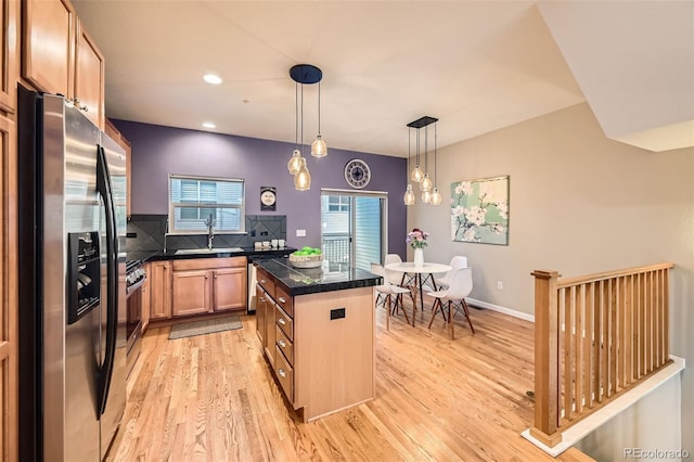 kitchen featuring a sink, a kitchen island, tasteful backsplash, stainless steel appliances, and light wood-style floors