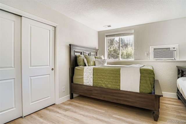 17630 E Loyola Dr Unit 1812L, Aurora, CO 80013 - bedroom with light wood finished floors, a textured ceiling, a wall unit AC, and a textured wall