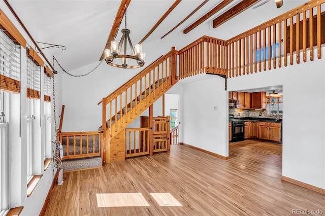 living room with a high ceiling, beam ceiling, light hardwood / wood-style flooring, an inviting chandelier, and sink