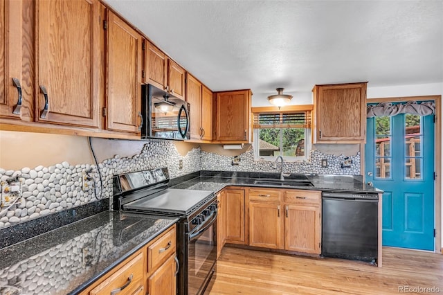 kitchen featuring sink, dark stone countertops, black appliances, and light hardwood / wood-style flooring