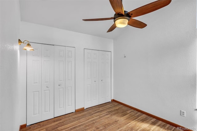 unfurnished bedroom featuring ceiling fan, wood-type flooring, and multiple closets