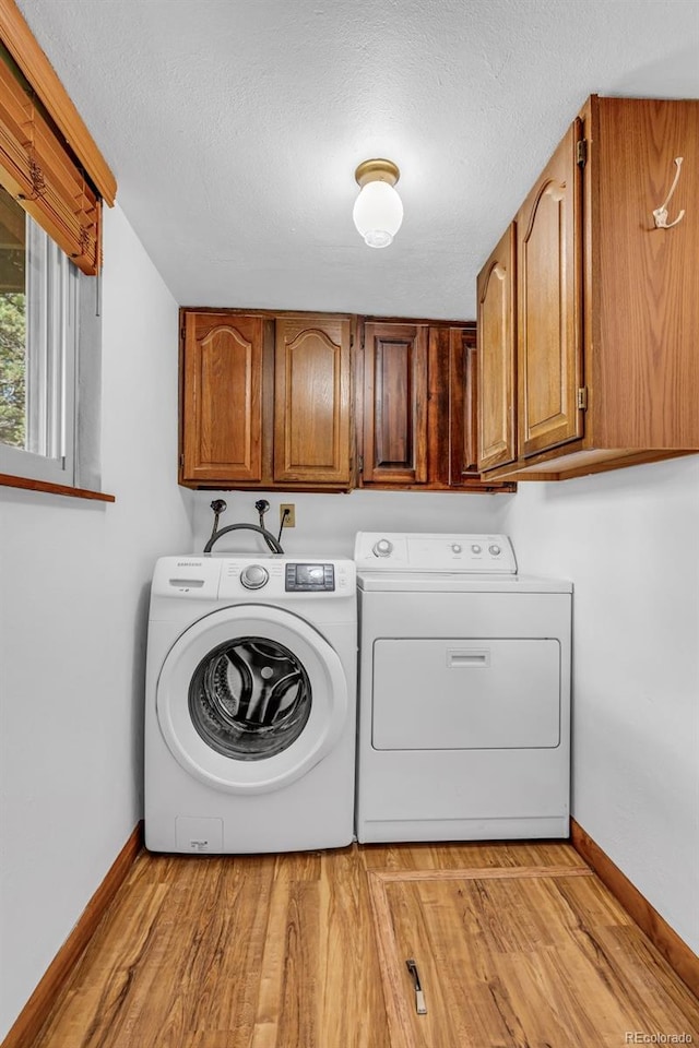 clothes washing area with a textured ceiling, cabinets, light hardwood / wood-style flooring, and washer and clothes dryer