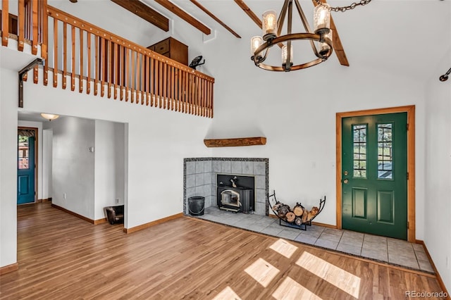 unfurnished living room featuring a chandelier, a high ceiling, a wood stove, beam ceiling, and wood-type flooring