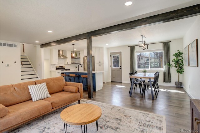 living area featuring stairway, beamed ceiling, wood finished floors, and visible vents