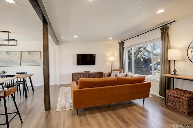 living room with a notable chandelier, recessed lighting, light wood-style floors, a textured ceiling, and baseboards