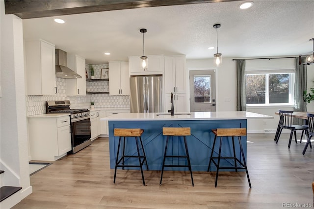 kitchen featuring stainless steel appliances, a sink, white cabinets, wall chimney range hood, and light wood finished floors